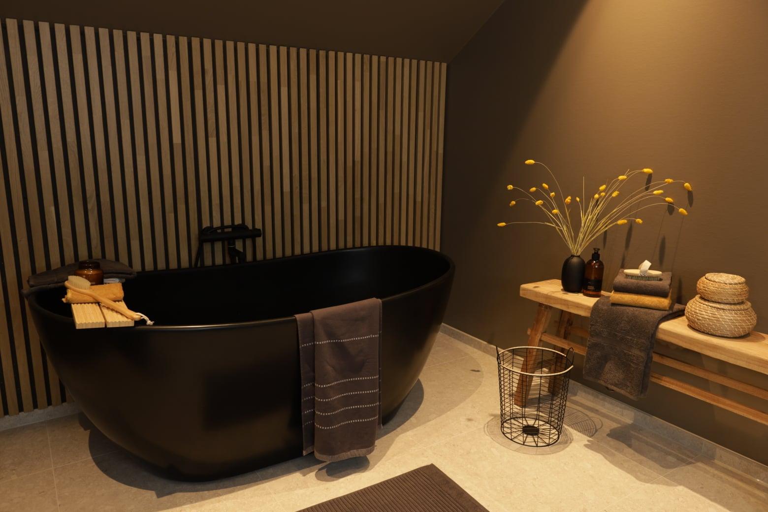 A dark freestanding bathtub against wooden slats, with a stool and dried flowers