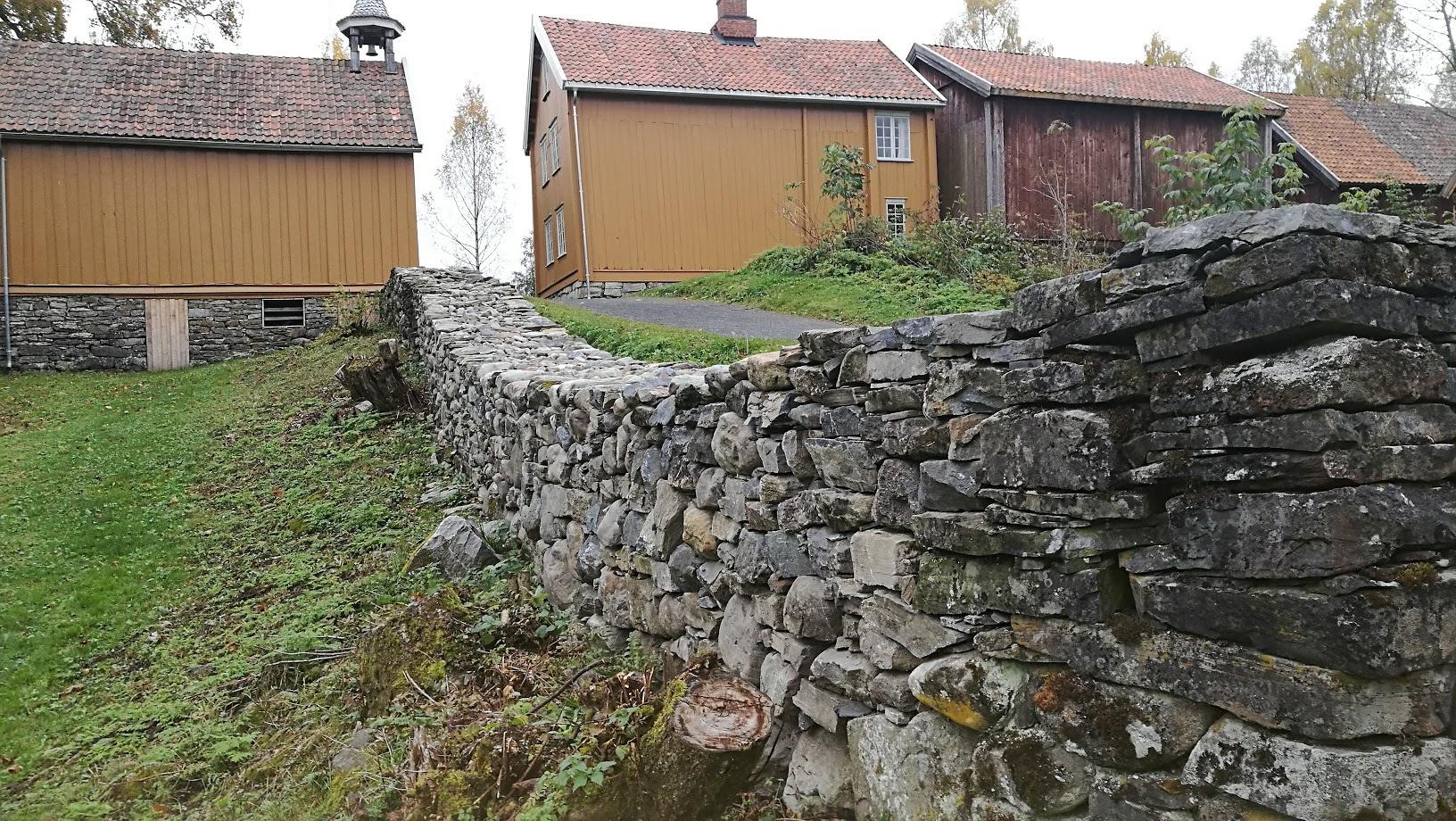 Old log farm buildings in ochre and red behind a dry-stone wall