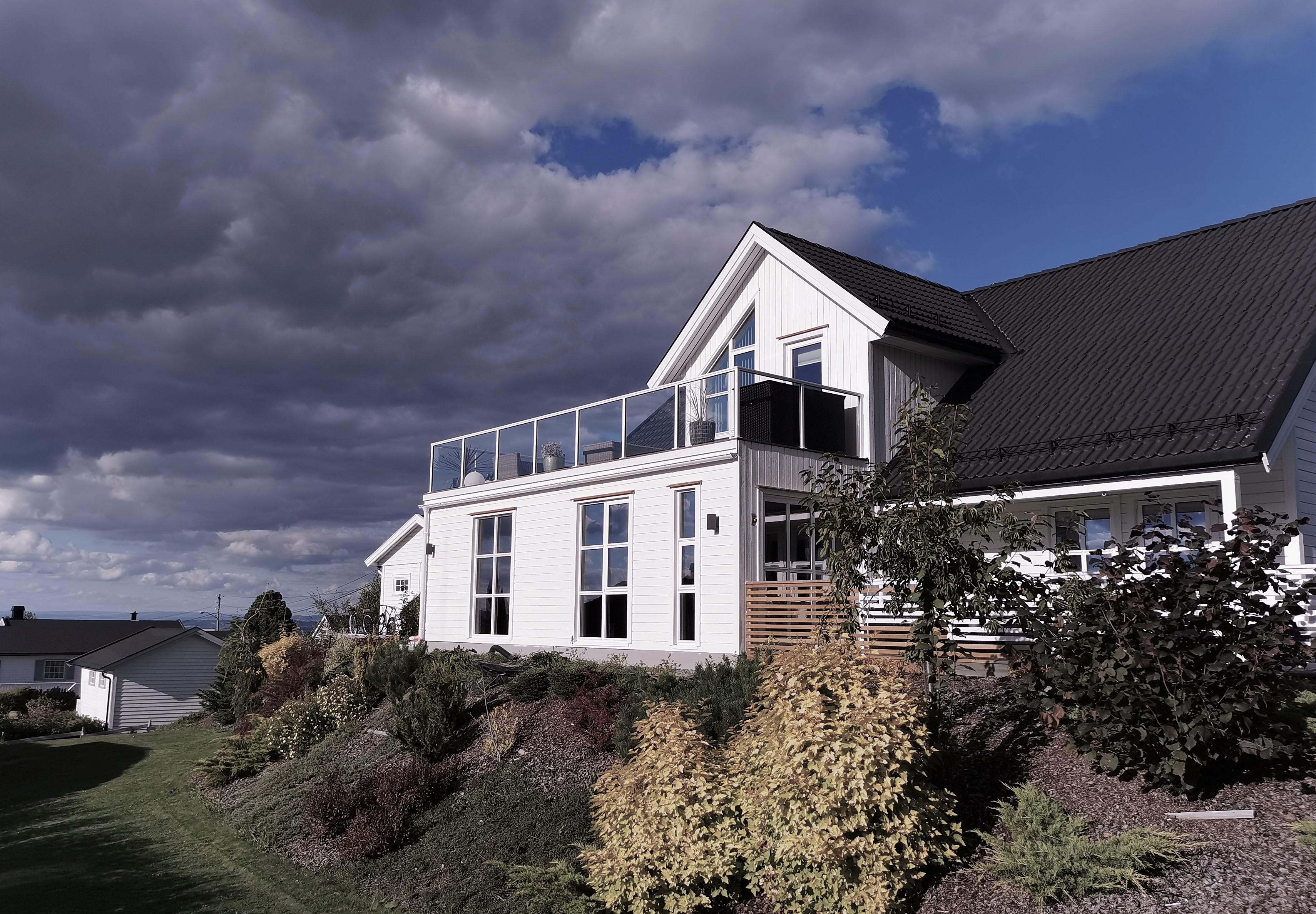 A white house with a glass balcony on a hillside under a stormy sky