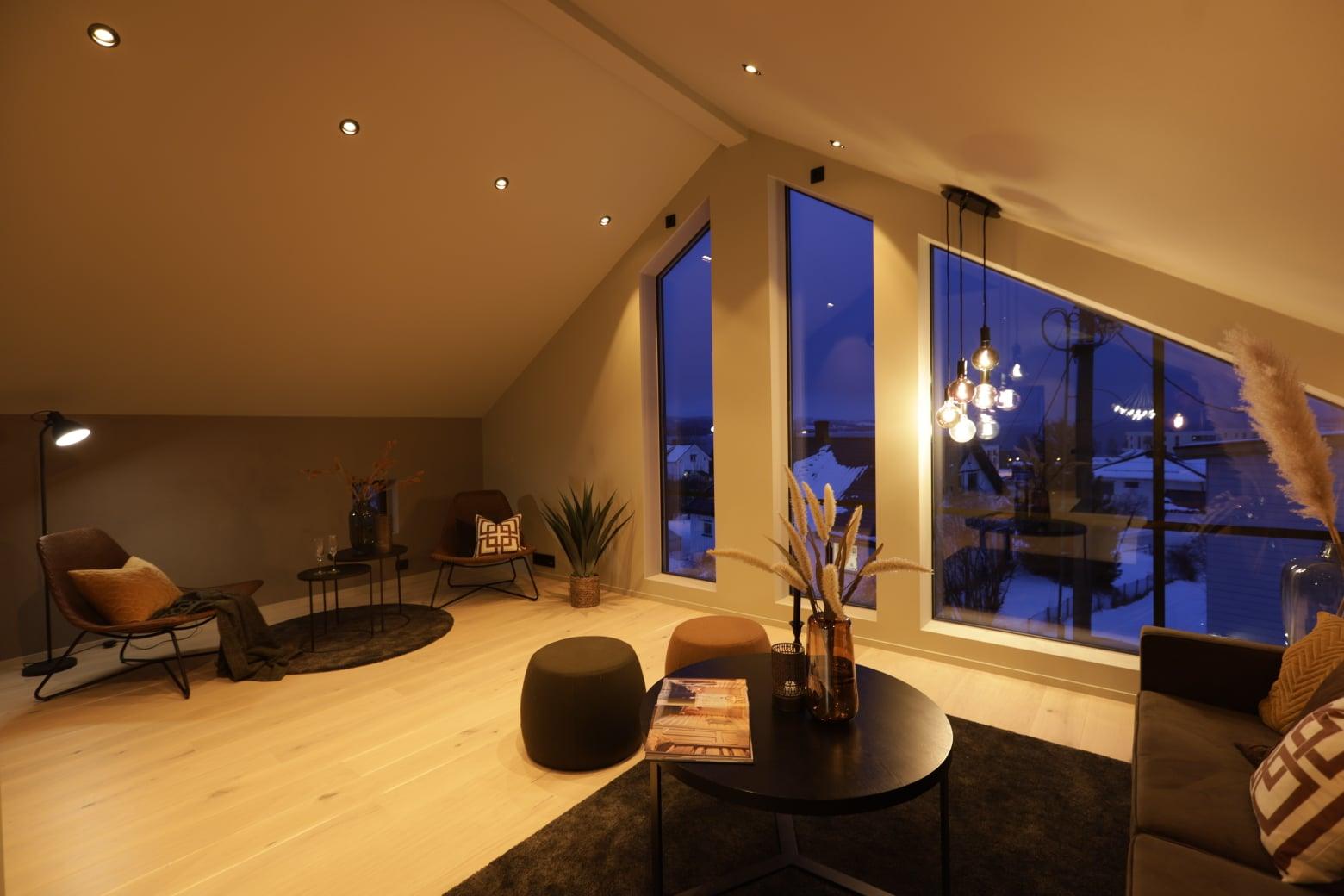 A living room under a pitched ceiling with tall windows at dusk