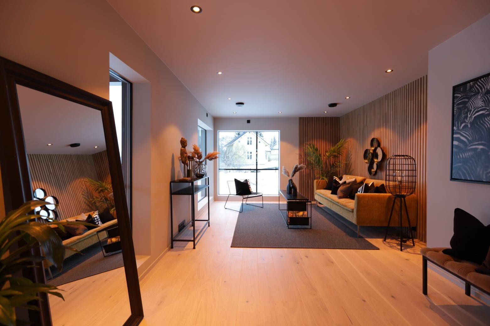 A long open living room with a wooden floor and a big mirror