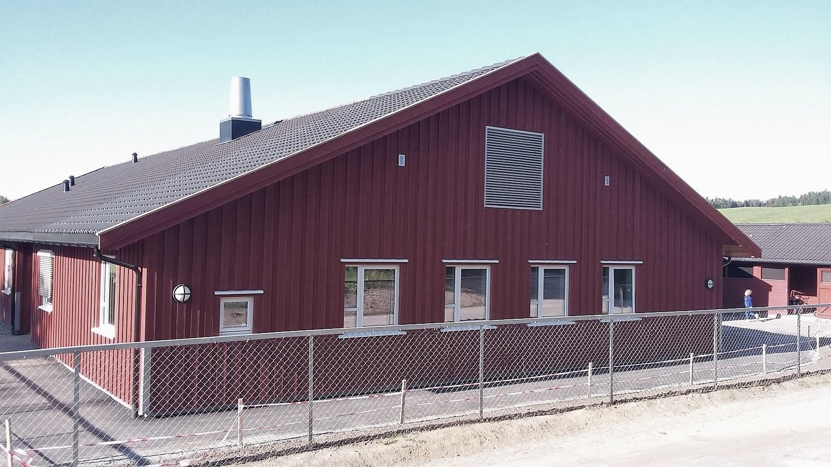 A long red timber building with a grey roof behind a fence